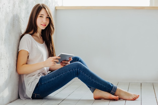 Belle fille assise près du mur et regarde dans la tablette