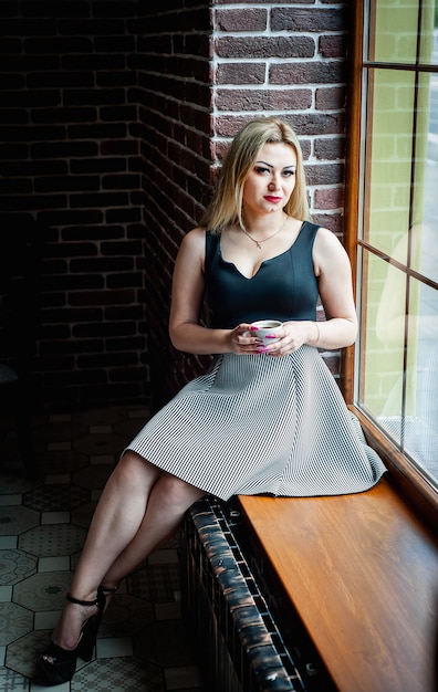 belle fille assise sur le rebord de la fenêtre près de la fenêtre avec une tasse de café, le bruit