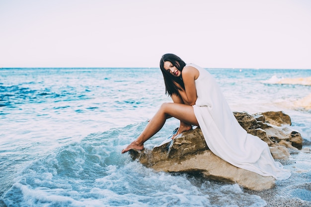 belle fille assise sur un rocher sur la mer de la plage