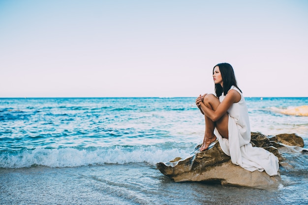 belle fille assise sur un rocher sur la mer de la plage