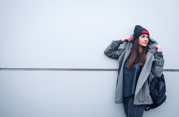 Belle fille athlétique aux cheveux noirs un bennie et un sac à dos sur fond de mur blanc