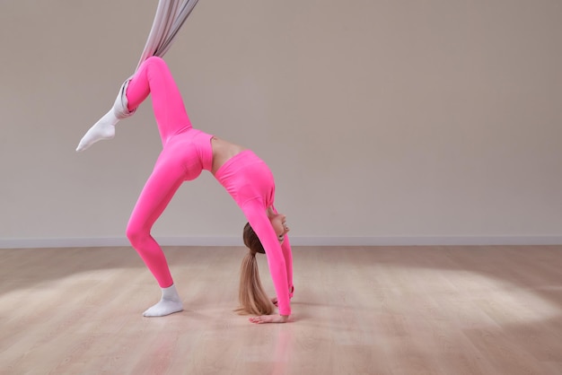 Belle fille athlétique dans un uniforme rose fait une pose de yoga et d'étirement d'air antigravité Le concept d'un mode de vie sain