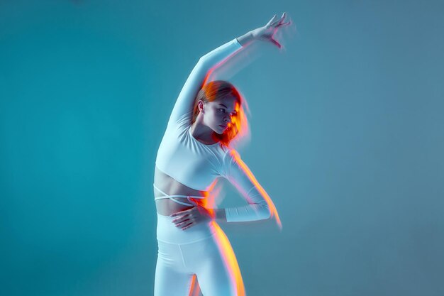 Une belle fille athlétique plie des figures isolées d'un modèle de fitness dans un uniforme de sport blanc