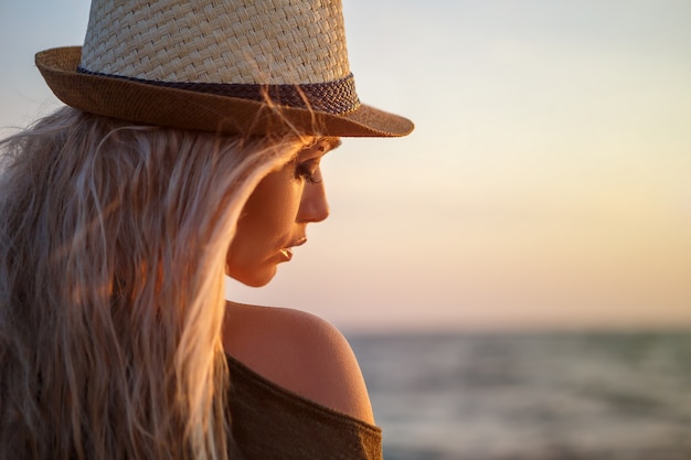 Belle fille au chapeau au bord de la mer au coucher du soleil.