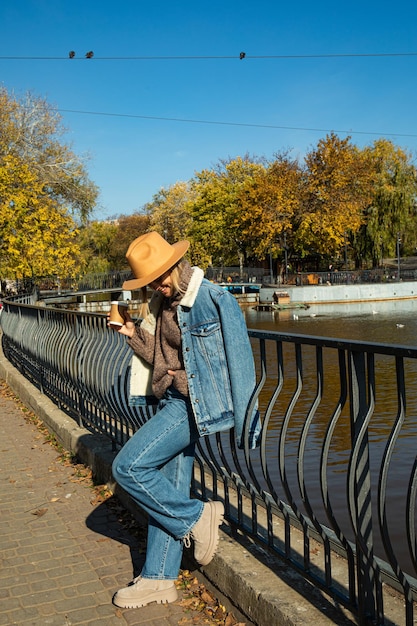 Une belle fille au chapeau se promène dans un parc en automne avec du café