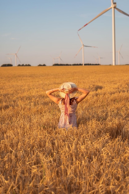 Belle fille au coucher du soleil dans un champ de blé avec des moulins à vent pour produire de l'électricité Le concept d'énergie renouvelable aime l'électricité de la nature Énergie renouvelable