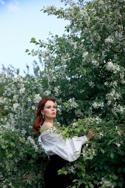 Belle fille au printemps dans les branches des buissons de pomme fleuris. Portrait d'une femme par un beau jour d'été