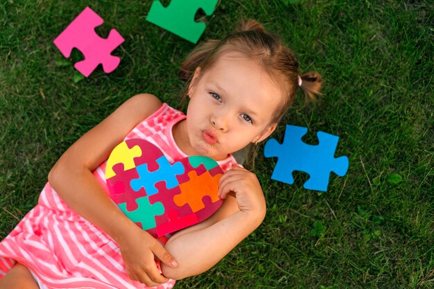 Une belle fille autiste souffle un baiser tout en tenant une carte décorée d'un puzzle