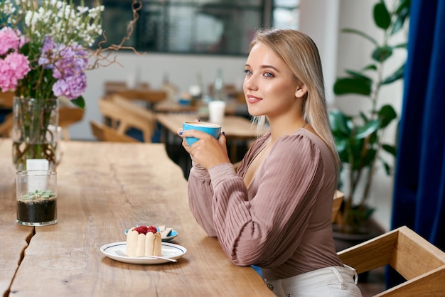 Belle fille aux cheveux blonds et aux yeux bleus buvant du café au café