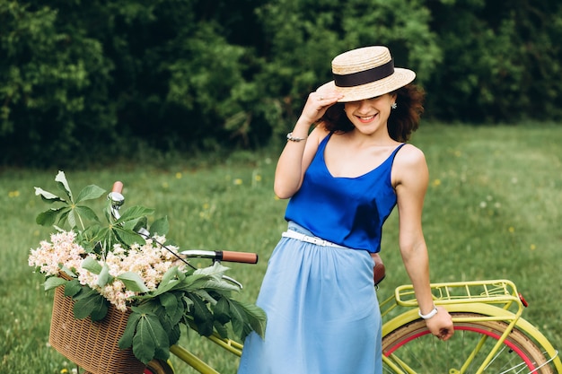 Belle fille aux cheveux bouclés dans un chapeau avec vélo avec panier de fleurs