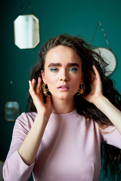 Une belle fille aux cheveux bouclés dans une robe rose Sur le fond des murs verts du studio de profil