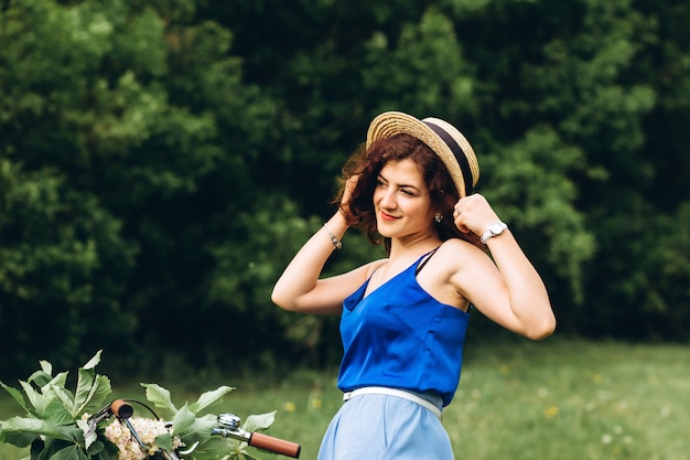 Belle fille aux cheveux bouclés détient vélo avec panier de fleurs et sourires