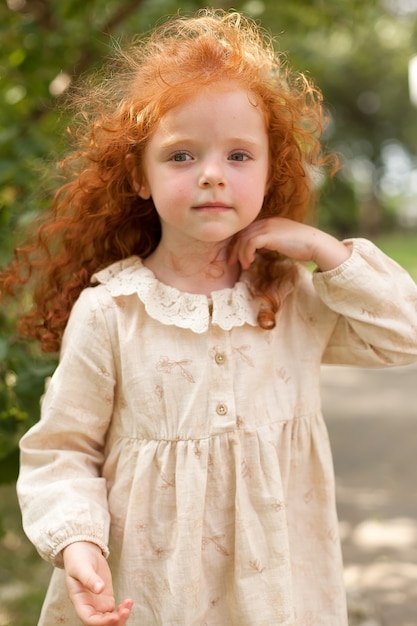 Belle fille aux cheveux bouclés rouges dans une robe violette posant parmi les fleurs sauvages dans un champ au coucher du soleil. Portrait.