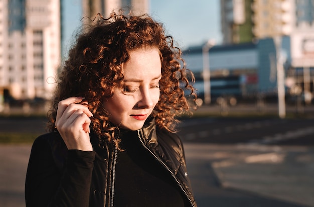 Belle fille aux cheveux bouclés sourit dans le contexte de la ville