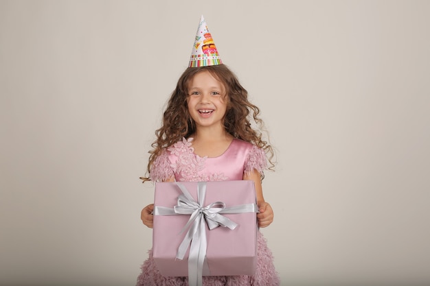 une belle fille aux cheveux bouclés vêtue d'une robe rose avec une boîte-cadeau dans les mains est un jour férié