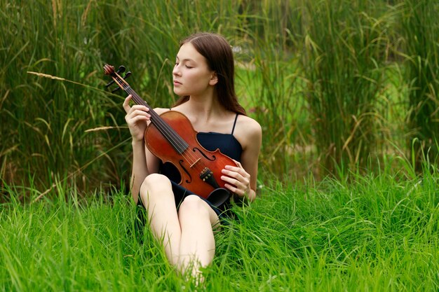 Belle fille aux cheveux bruns d'apparence asiatique avec un violon dans la nature. musicien de nature. musique classique. photo de haute qualité