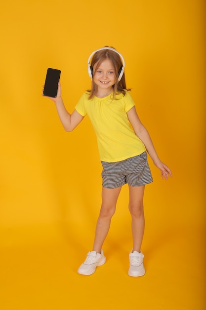 une belle fille aux cheveux bruns dans un short Tshirt jaune portant des écouteurs avec un téléphone