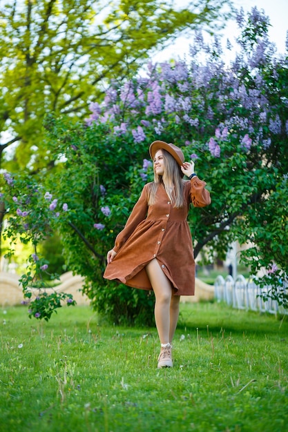 Belle fille aux cheveux longs dans un chapeau sur fond de fleurs lilas. Elle a une apparence européenne avec un sourire sur son visage. Jeune femme marchant par une chaude journée ensoleillée dans un parc fleuri