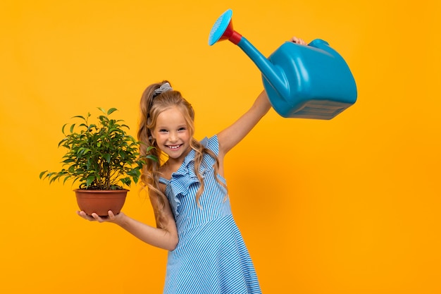 Belle fille aux cheveux longs détient une plante et sourit, photo isolée sur jaune