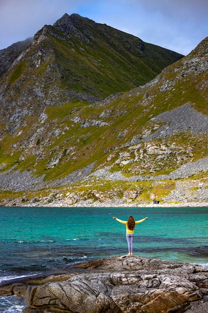 belle fille aux cheveux longs lève les mains en l'air sur la célèbre plage paradisiaque de haukland, norvège