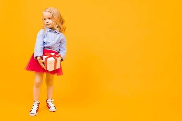 Belle fille aux cheveux longs sourit et détient un cadeau, photo isolé sur jaune