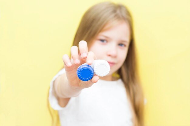 Une belle fille aux cheveux longs tient un récipient avec des lentilles à la main. Le concept de problèmes de vision chez les enfants. Fond jaune.