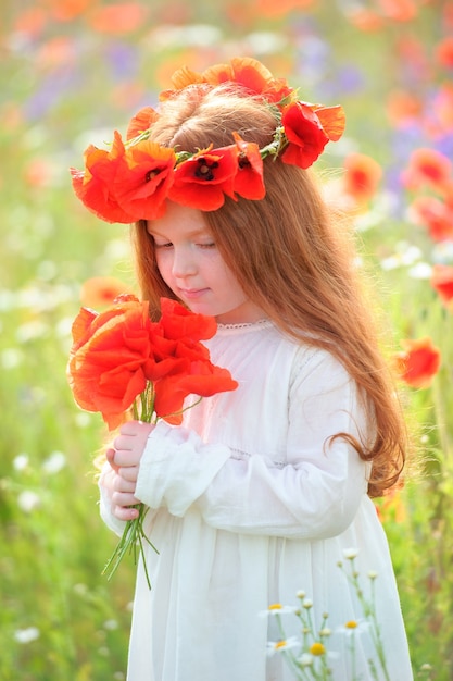 Belle fille aux cheveux d'or dans une robe blanche et un bouquet de fleurs sauvages