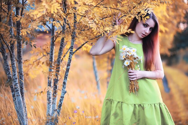 Belle fille aux cheveux rouges avec un bouquet de marguerites sur la nature