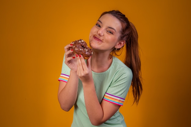 Belle fille aux cheveux roux mangeant des beignets au chocolat sur fond jaune. fille mangeant des beignets