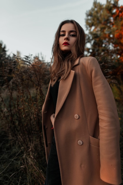 Belle fille aux lèvres rouges dans des vêtements à la mode avec un long manteau classique sur la nature