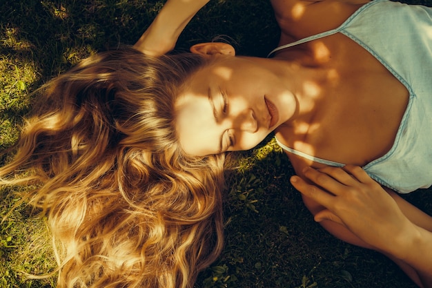 Une belle fille aux longs cheveux blancs repose sur un gazon vert et sourit. Strabisme. Un œil rétréci et un sourire sournois.