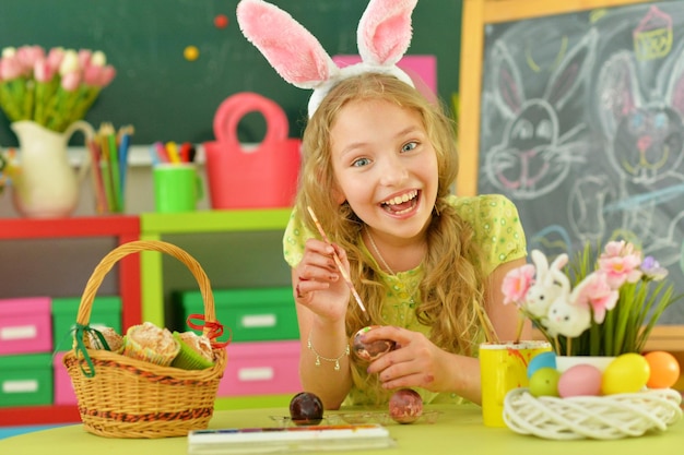 Belle fille aux oreilles de lapin peignant des oeufs pour les vacances de Pâques