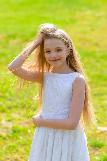 Belle fille aux yeux bleus avec de longs cheveux blonds dans une robe blanche marche jardin fleuri. Été et printemps photo lumineuse et émouvante.