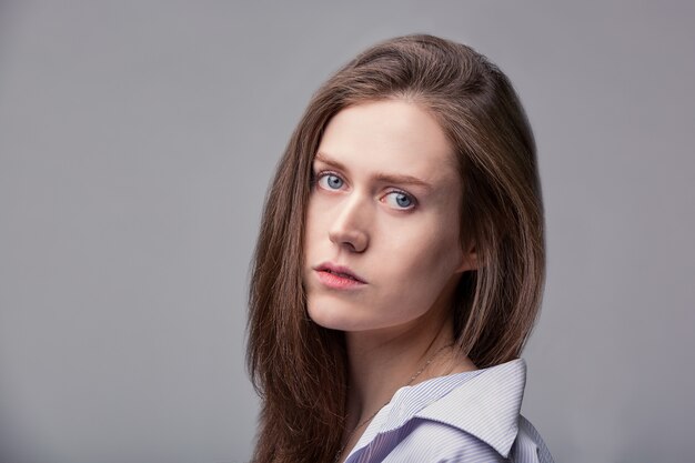 Belle fille aux yeux bleus posant sur un espace gris