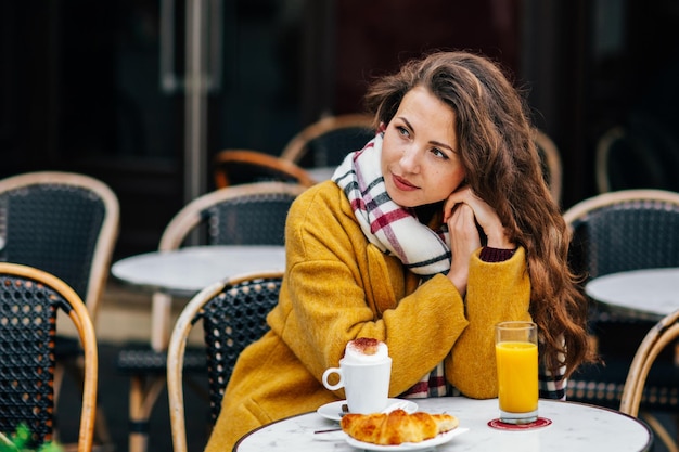 Belle fille bien roulée dans un café parisien dans un manteau jaune boit du café à Paris