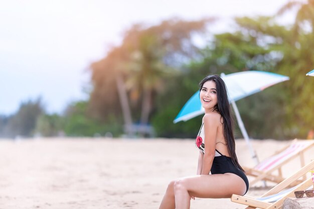 Photo belle fille en bikini reposant sur une chaise longue sous un parasol près de la mer