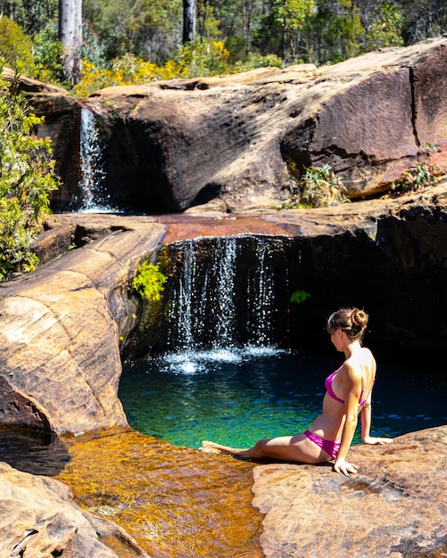 belle fille en bikini rose est assise près d'une piscine de roche naturelle avec des chutes d'eau dans le plateau de blackdown