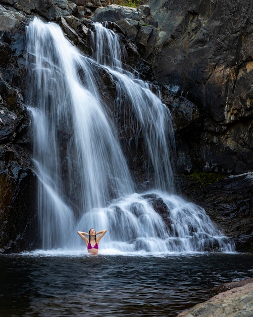 une belle fille en bikini rose se tient sous une cascade dans une piscine naturelle, queensland, australie