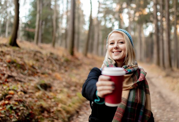 Belle fille blonde au chapeau bleu avec une tasse de café dans une forêt