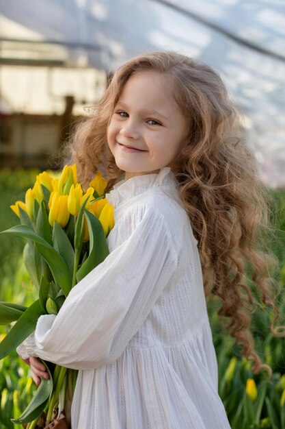 une belle fille blonde aux cheveux longs dans un chemisier blanc tient un bouquet de tulipes jaunes dans ses mains