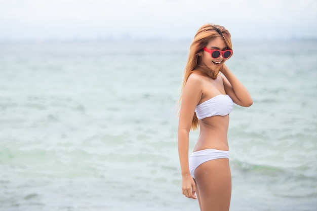 Belle fille blonde en bikini blanc se tenir sur la plage.