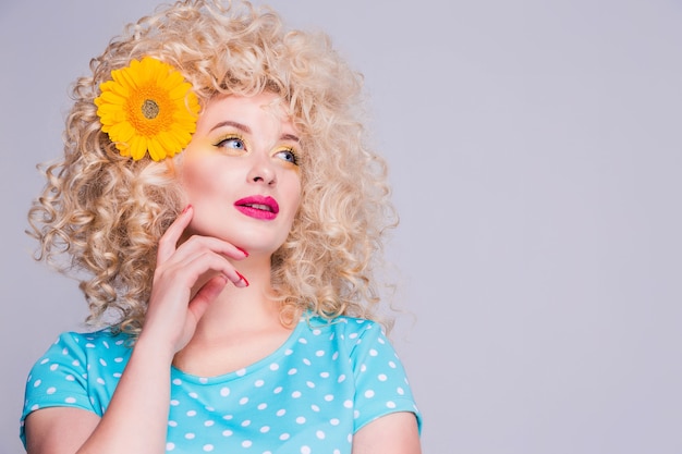 Belle fille blonde avec une coiffure frisée volumineuse, dans un chemisier à pois bleu