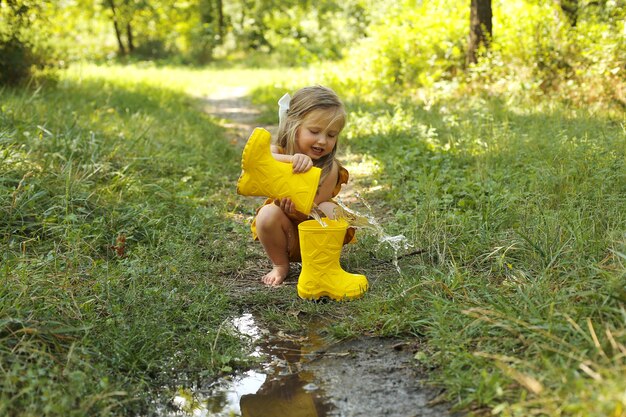 Photo une belle fille blonde dans un costume de lin couleur moutarde verse de l'eau d'une botte jaune