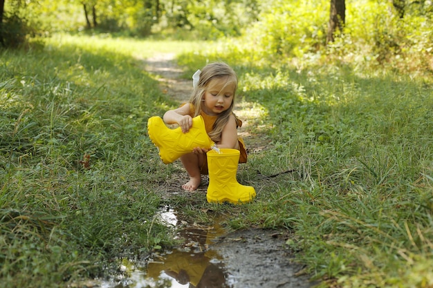 une belle fille blonde dans un costume de lin couleur moutarde verse de l'eau d'une botte jaune