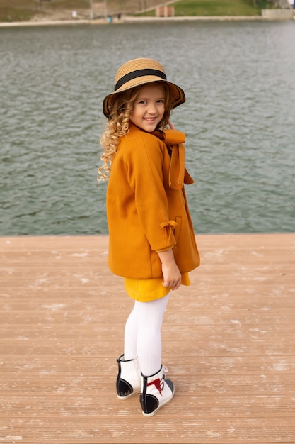 une belle fille blonde dans un manteau beige avec un chapeau sur la jetée de la nature du lac de la ville