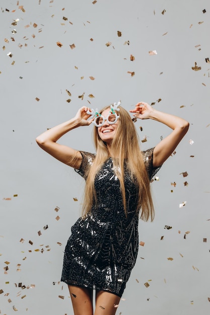 Une belle fille blonde danse sous le concept de fête du nouvel an de confettis scintillants