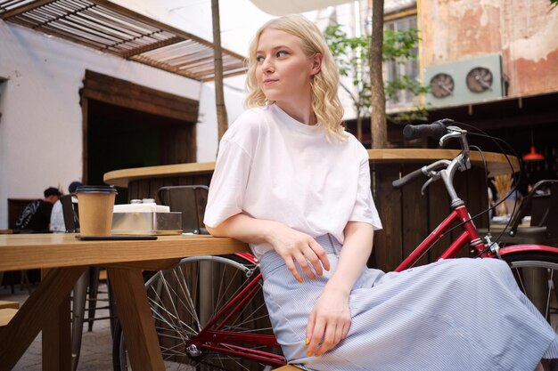 Belle fille blonde décontractée regardant pensivement tout en se reposant seule dans la cour du café