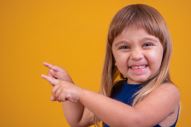 Belle fille blonde enfant souriante regardant la caméra pointant sur le côté.