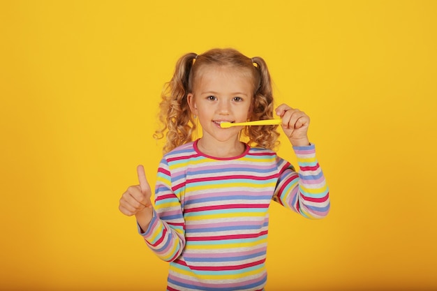 une belle fille blonde sur fond jaune dans une veste colorée avec une brosse à dents