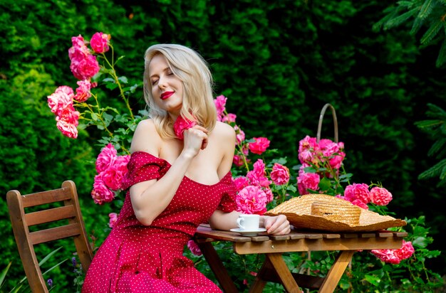 Belle fille blonde en robe rouge, boire un café dans un jardin